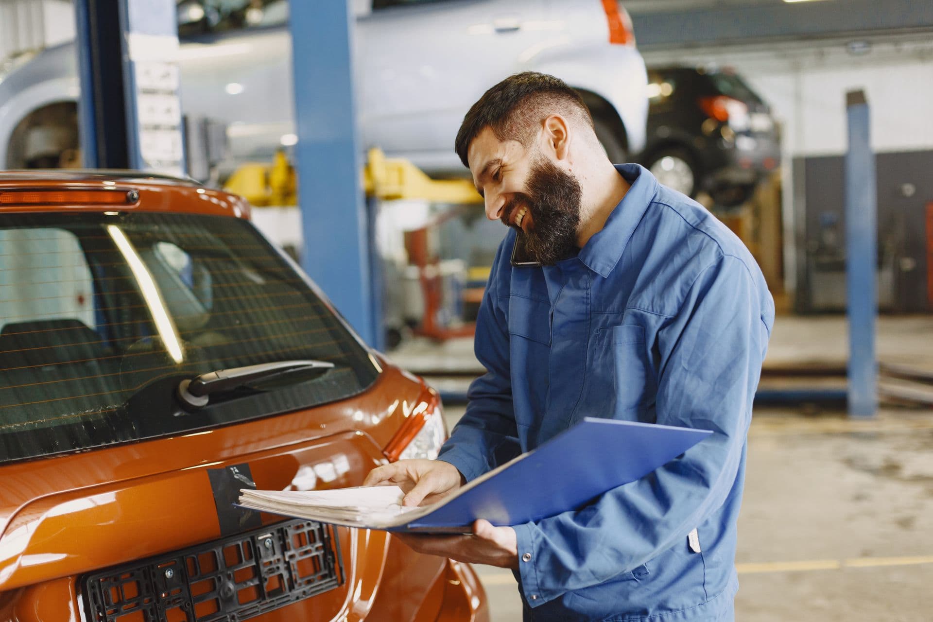 Mecanic într-un service auto vorbind la telefon cu un client, zâmbind